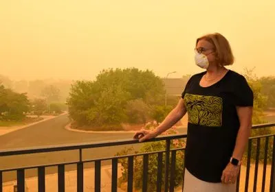 woman in mask on balcony looks at smoky landscape 